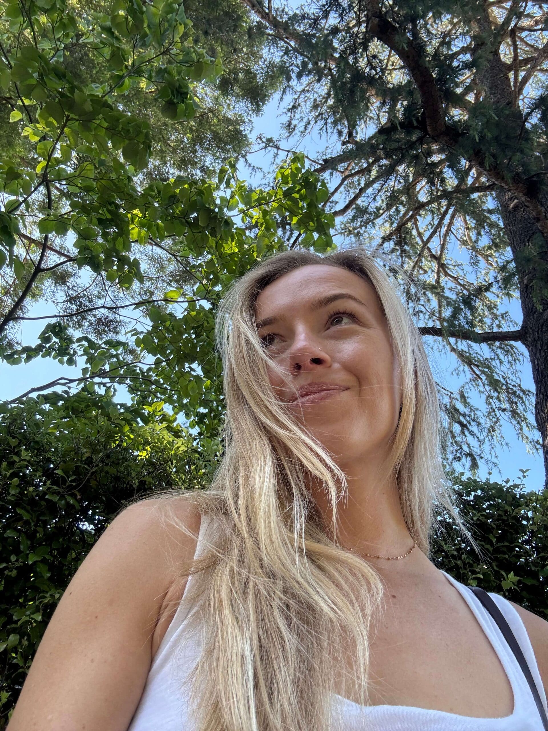 Woman smiling looking up at trees behind her